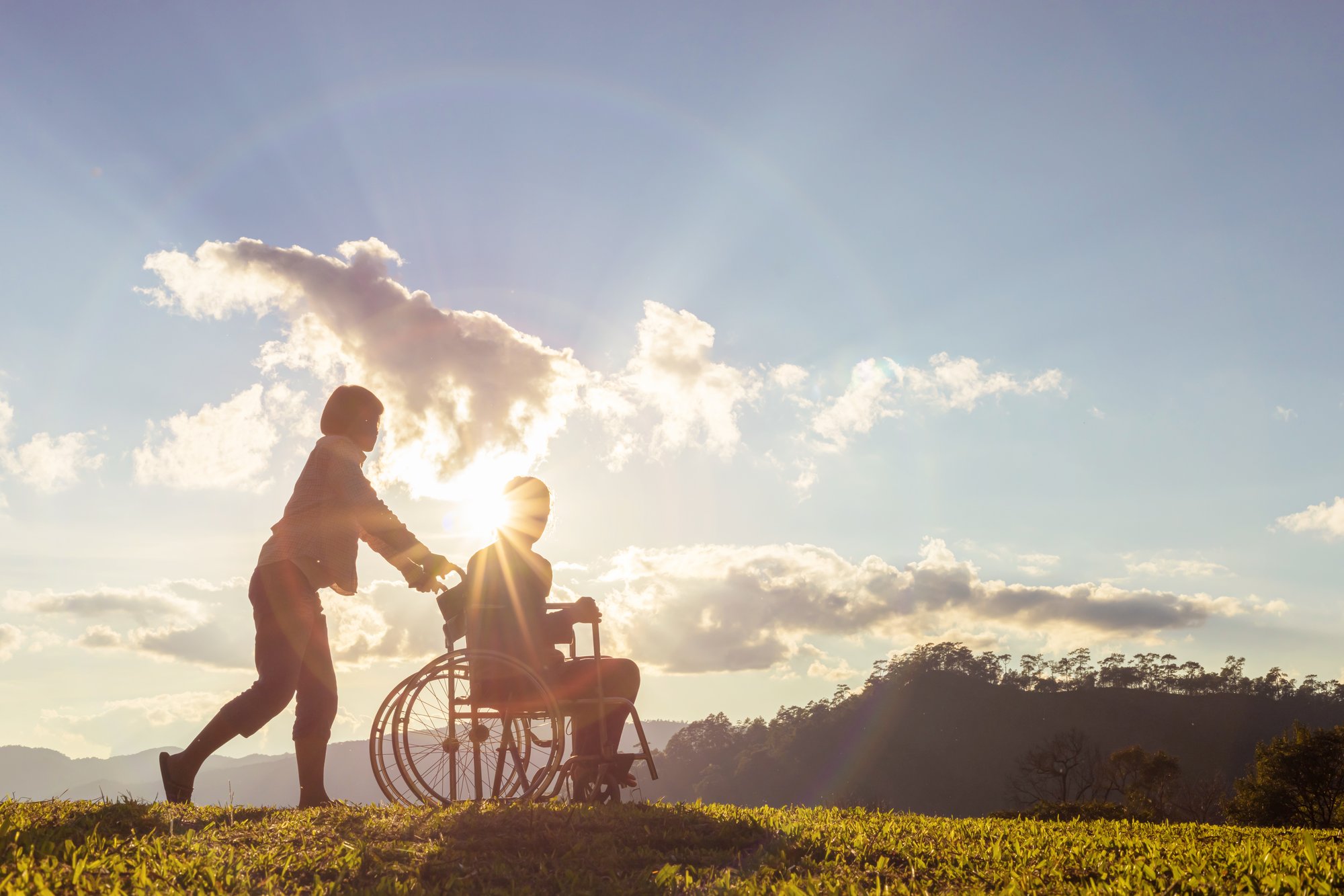 Person in wheelchair being pushed by nurse against bright sunlight