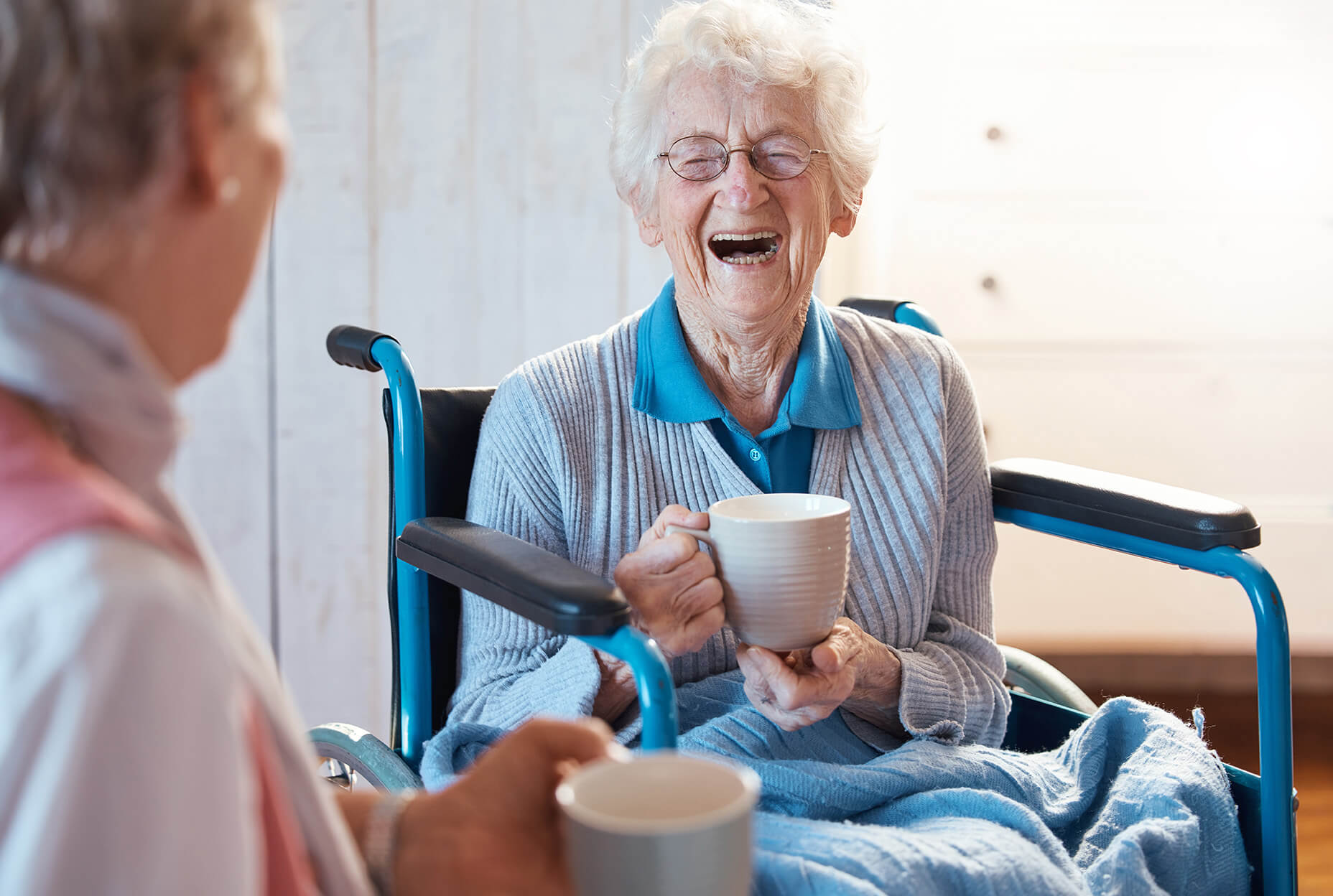 Two older women laughing together while drinking tea